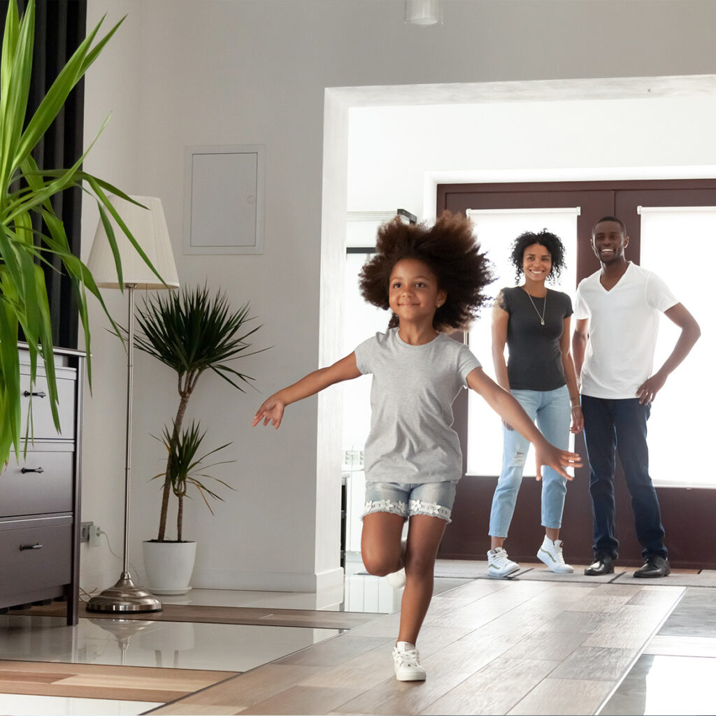 a little girl running through her home while her parents watch from the entry way