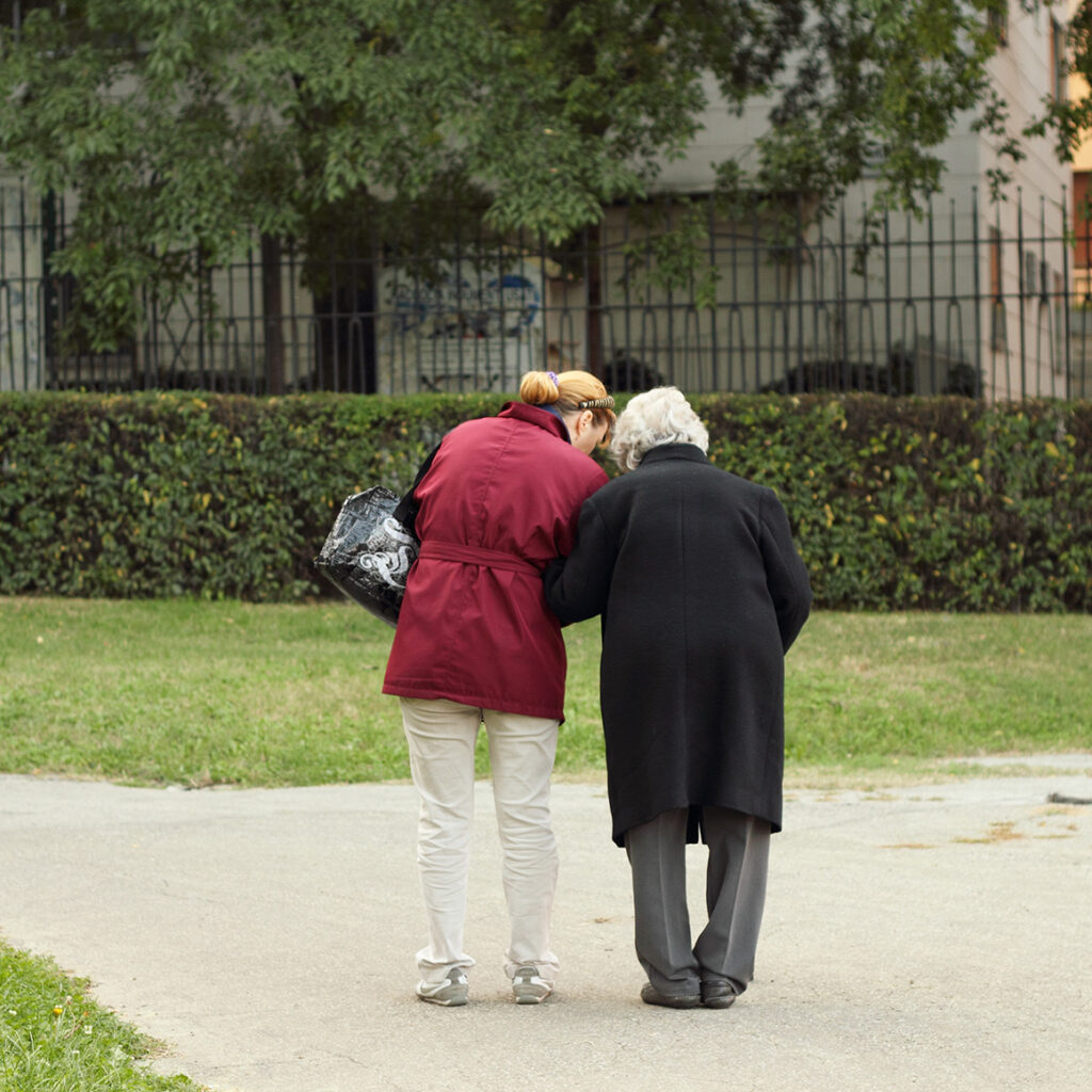 a younger woman helping an elderly woman walk through the park